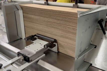 Stapel aus Wellpappe wird in einer industriellen Schneidemaschine seitlich ausgerichtet und fixiert.