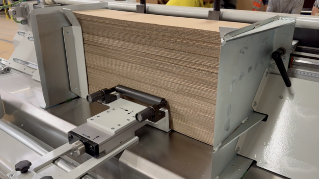 Stapel aus Wellpappe wird in einer industriellen Schneidemaschine seitlich ausgerichtet und fixiert.