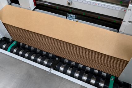 Kolibri Schneidemaschine schneidet einen Stapel Wellpappe präzise über rotierende Walzen in einer industriellen Produktionsanlage