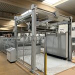 Seitliche Ansicht der Schneidanlage mit Förderbereich und Schutzgitter in industrieller Umgebung.