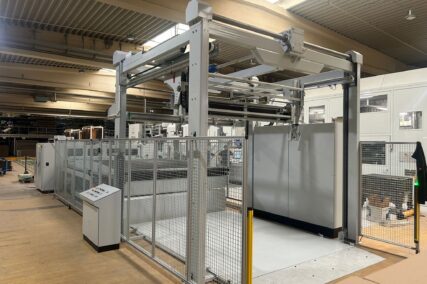Seitliche Ansicht der Schneidanlage mit Förderbereich und Schutzgitter in industrieller Umgebung.