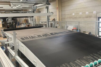 Förderband der Anlage mit aufliegendem Material vor dem Schneidprozess in einer Produktionshalle.