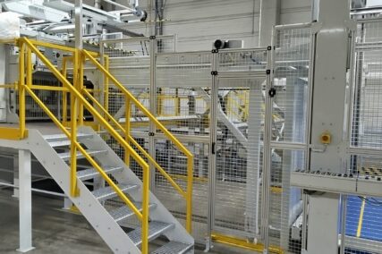 Seitlicher Zugang zur Anlage mit gelbem Treppenaufgang, Wartungspodest und Schutzgittern.