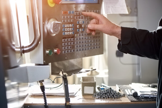 Hand eines Mitarbeiters bei der Bedienung des Steuerpanels einer CNC-Maschine in der Metallverarbeitung.