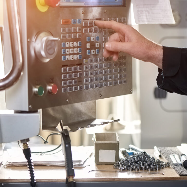 Hand eines Mitarbeiters bei der Bedienung des Steuerpanels einer CNC-Maschine in der Metallverarbeitung.