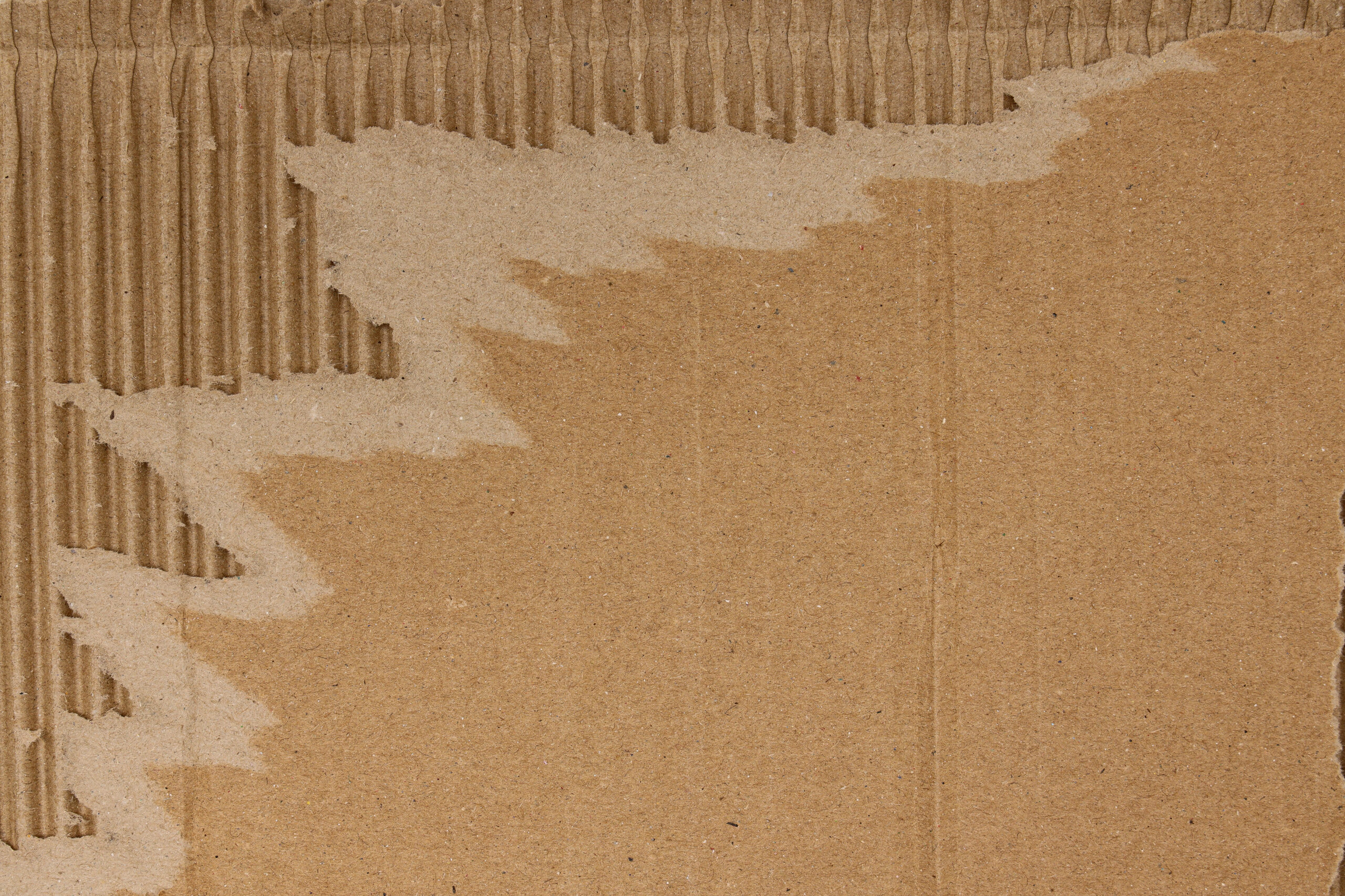 Strukturierte Kartonoberfläche mit freigelegter Wellpappe und sichtbaren Materialfasern.