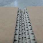 Nahaufnahme von Wellpappe mit geöffneter Schnittkante. In der Mitte ist die typische gewellte Papierstruktur zwischen zwei glatten Kartonschichten sichtbar.