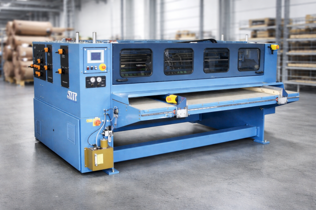 Industrielle Kreisschere V (Notch Fold) zur Bearbeitung von Wellpappe in einer Produktionshalle. Die blaue Maschine mit Bedienpanel, Sichtfenstern und Zuführtisch dient zum Schneiden und Rillen von Wellpappzuschnitten.