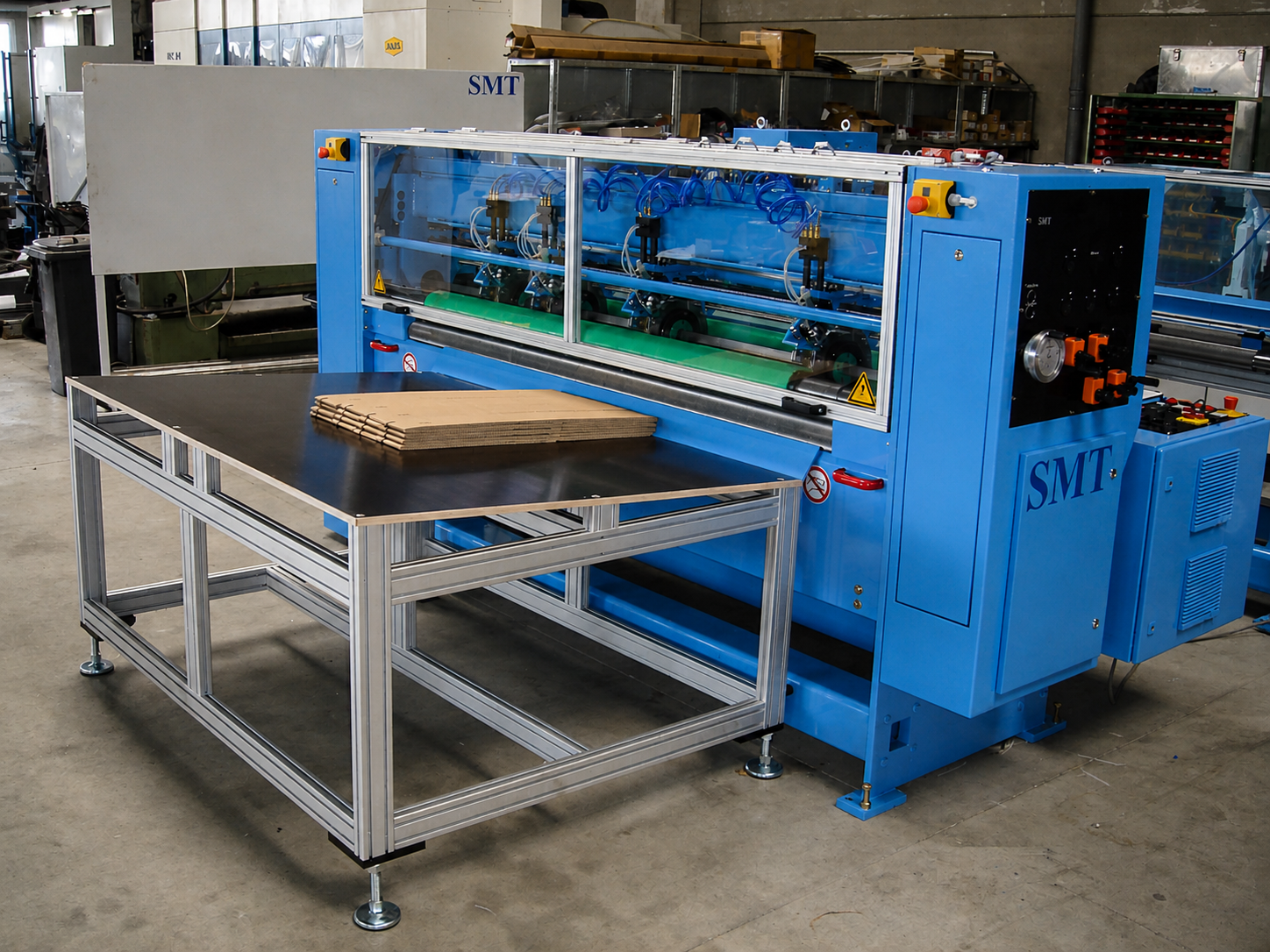 Gesamtansicht der CDS-ECO Schneidemaschine von SMT mit integriertem Zuführtisch und aufgelegtem Wellpappenstapel in einer industriellen Produktionsumgebung