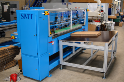 Gesamtansicht der CDS-ECO Schneidemaschine von SMT mit integriertem Zuführtisch und aufgelegtem Wellpappenstapel in einer industriellen Produktionsumgebung