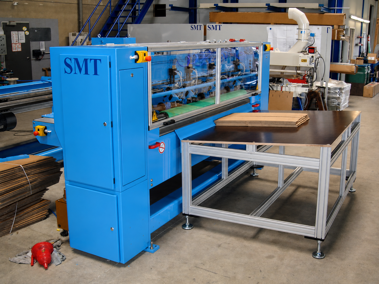 Gesamtansicht der CDS-ECO Schneidemaschine von SMT mit integriertem Zuführtisch und aufgelegtem Wellpappenstapel in einer industriellen Produktionsumgebung