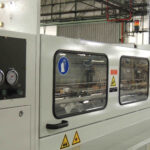 Maschinengehäuse der Kolibri Schneidemaschine mit mehreren Sichtfenstern, Druckanzeigen und Sicherheitshinweisen in einer Produktionshalle