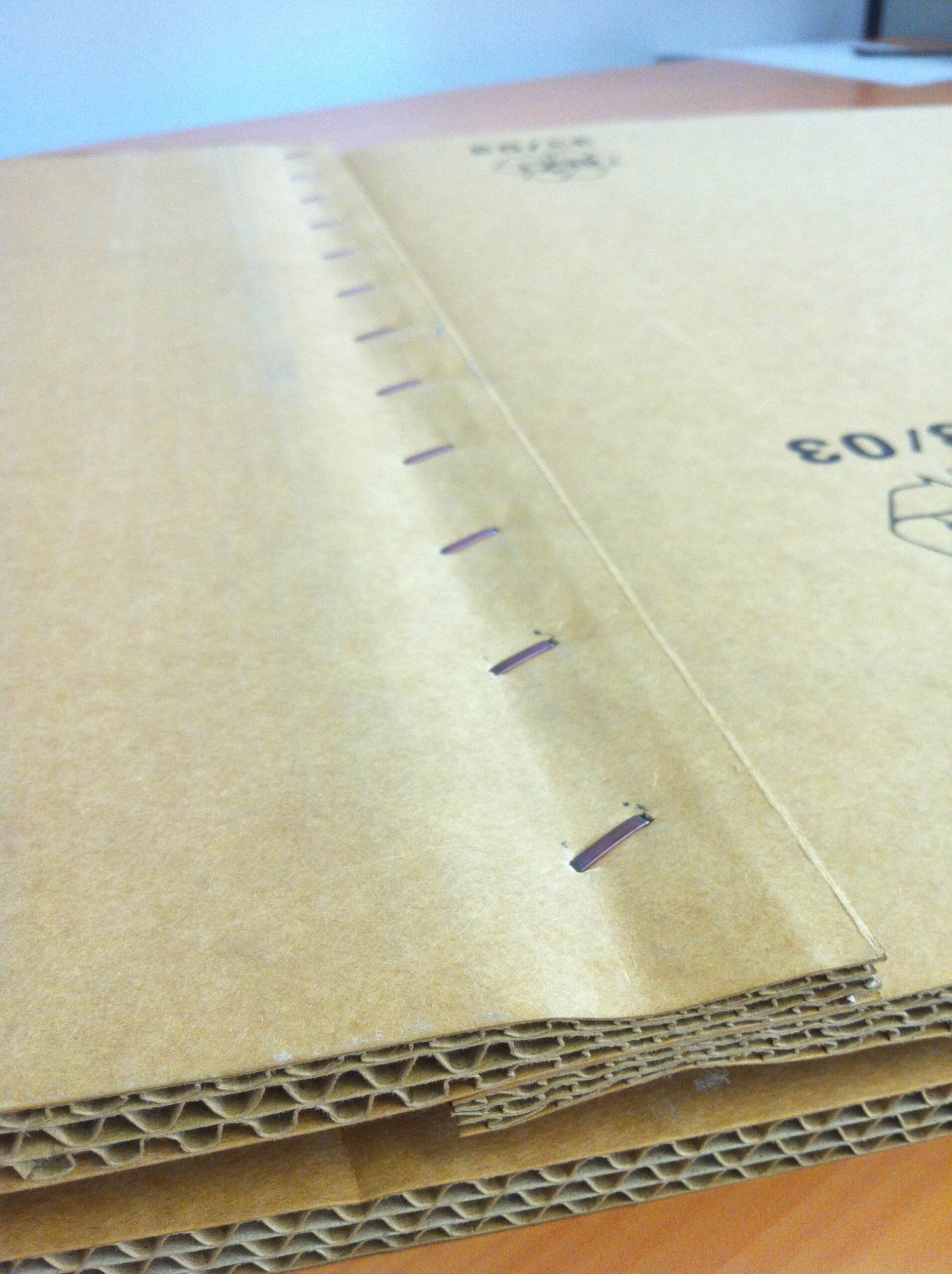 Detailaufnahme von gefalteter Wellpappe mit sichtbarer Heftung entlang der Kante in der Weiterverarbeitung
