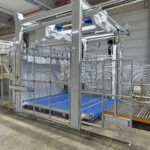 Gesamtansicht der Kolibri Schneidemaschine mit Schutzgitter, Fördertechnik und automatisierten Komponenten in einer industriellen Umgebung