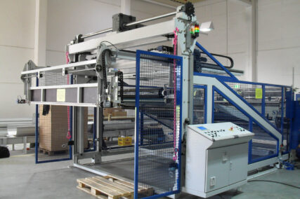 Gesamtansicht einer Upstacker Anlage zur Wabenplattenproduktion mit Schutzgitter, Rollen und Bedienpult in einer industriellen Produktionshalle
