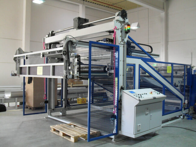 Gesamtansicht einer Upstacker Anlage zur Wabenplattenproduktion mit Schutzgitter, Rollen und Bedienpult in einer industriellen Produktionshalle