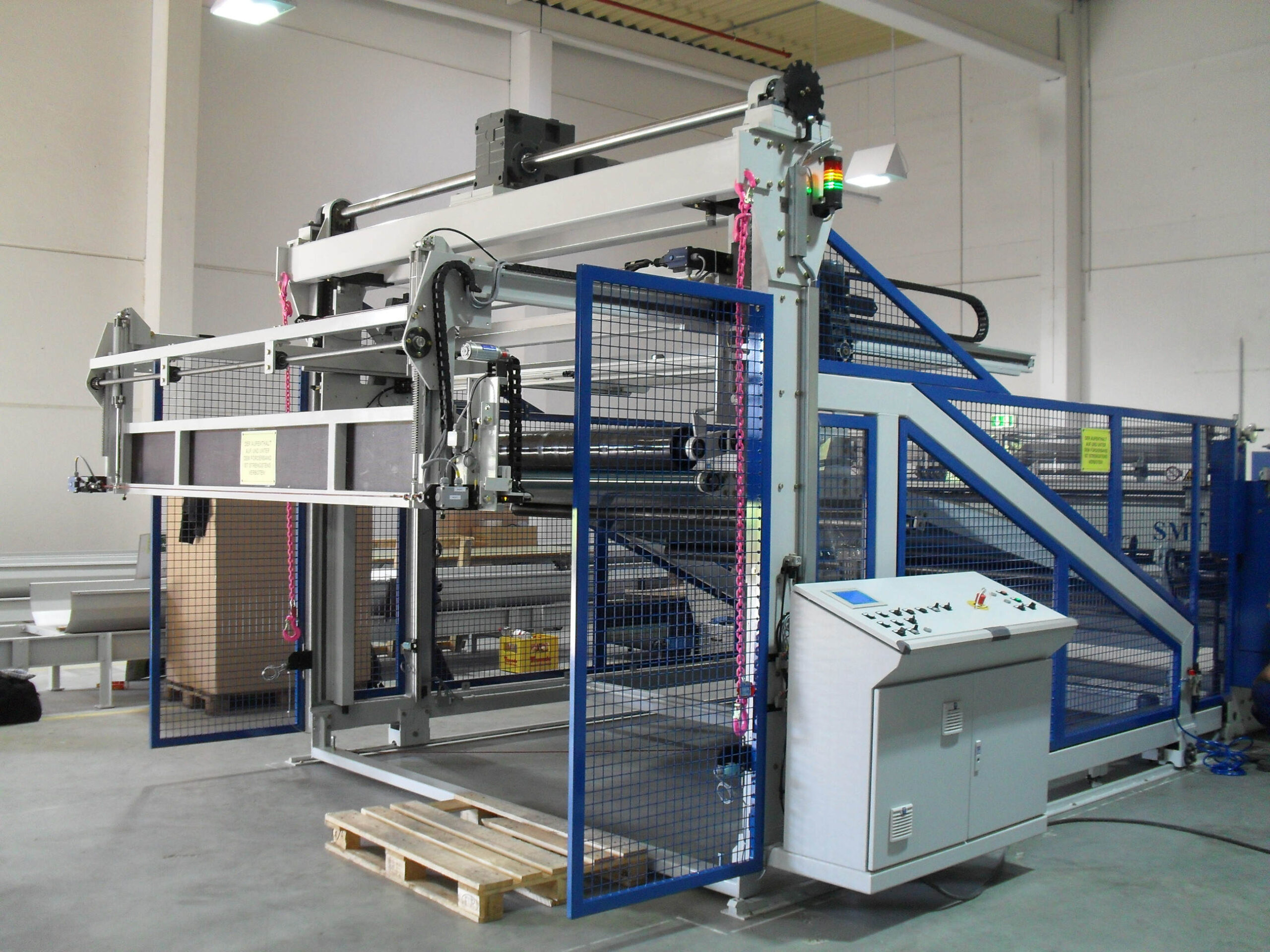 Gesamtansicht einer Upstacker Anlage zur Wabenplattenproduktion mit Schutzgitter, Rollen und Bedienpult in einer industriellen Produktionshalle